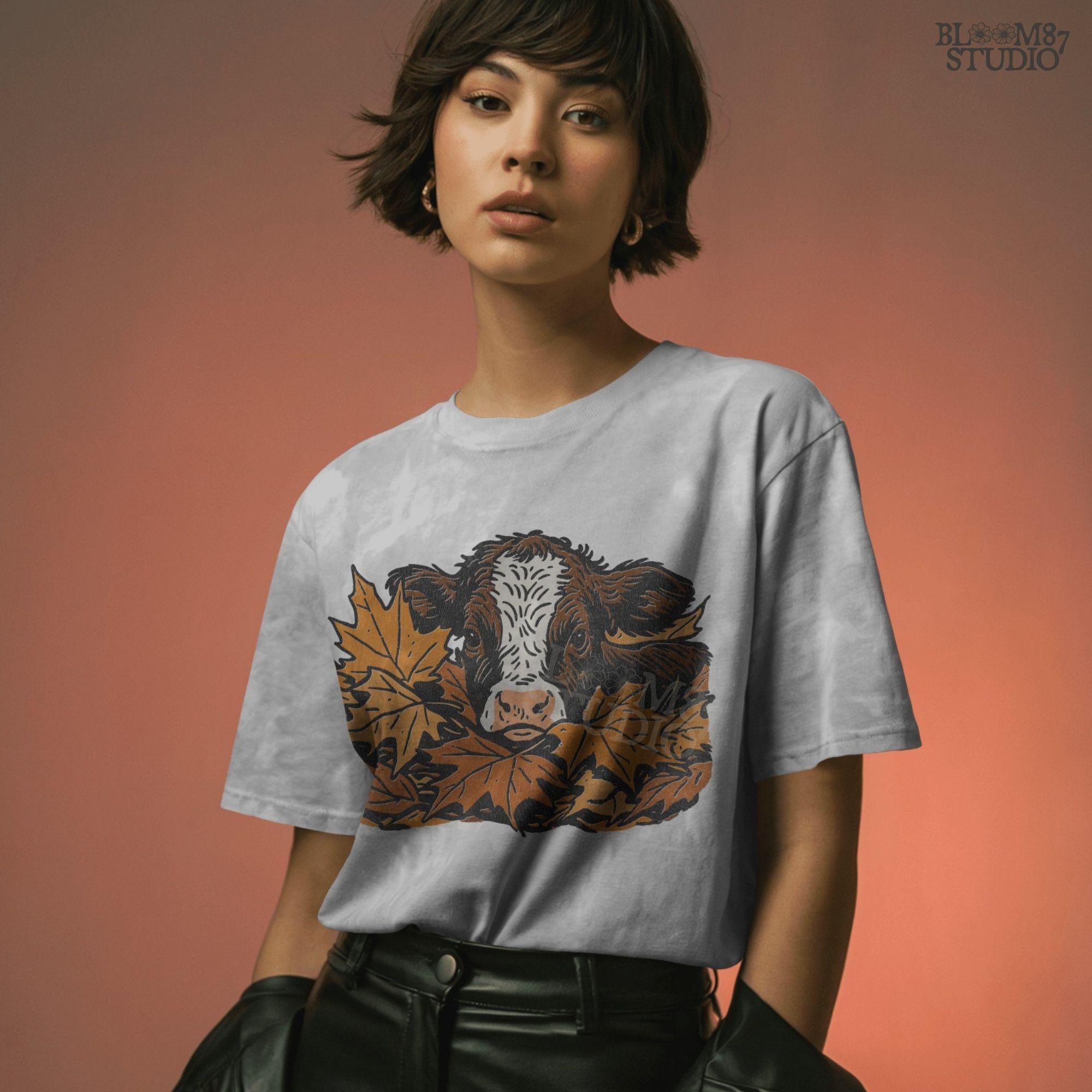 Cute brown and white highland calf resting in a pile of orange and brown fall maple leaves, perfect for autumn sublimation projects