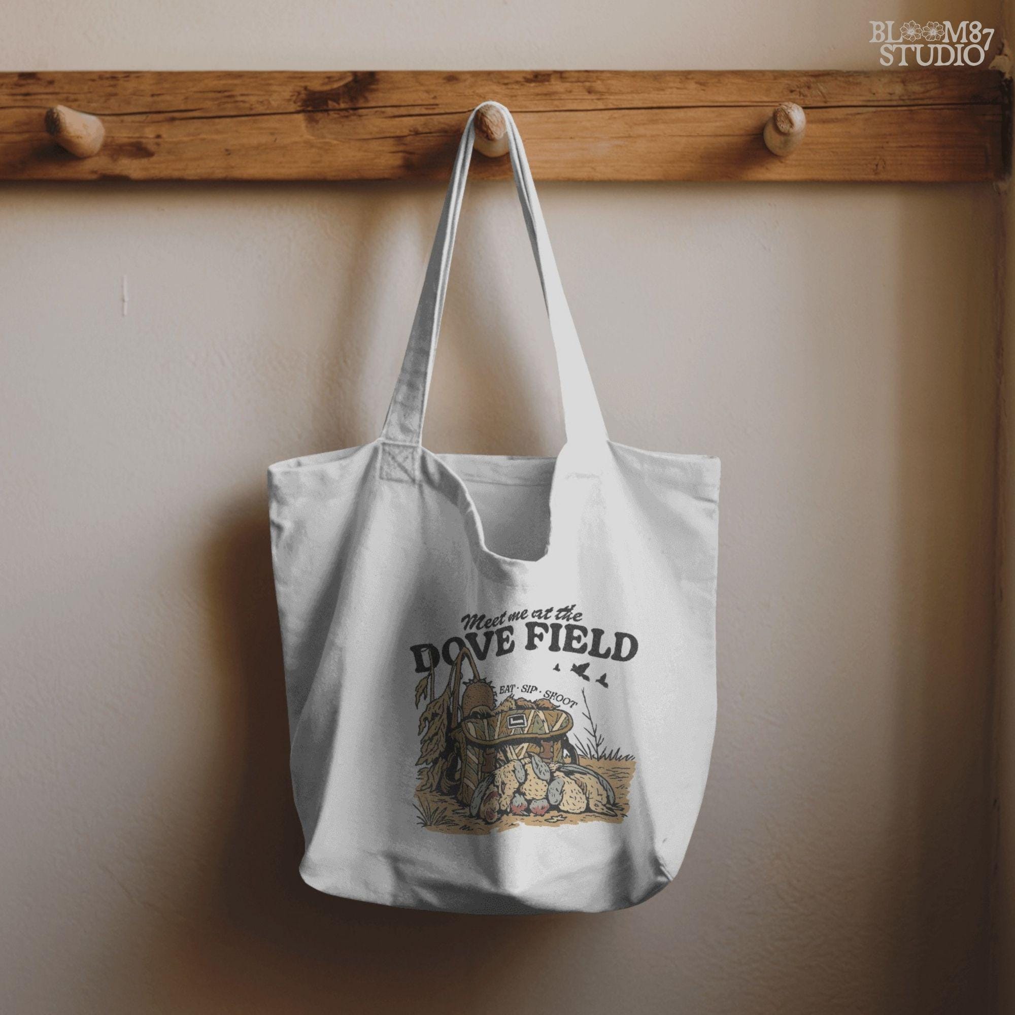 Camo hunting bag in a cornfield surrounded by harvested mourning doves with the phrase “Meet Me at the Dove Field” in vintage lettering.