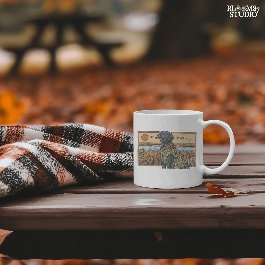 Camo-clad black Labrador retriever sitting in a grassy marsh with flying ducks and a sunset background, digital PNG for hunting dog sublimation designs.
