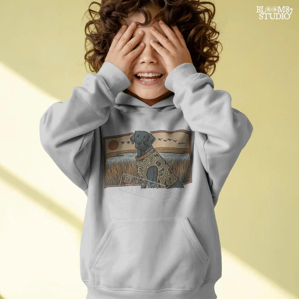 Camo-clad black Labrador retriever sitting in a grassy marsh with flying ducks and a sunset background, digital PNG for hunting dog sublimation designs.