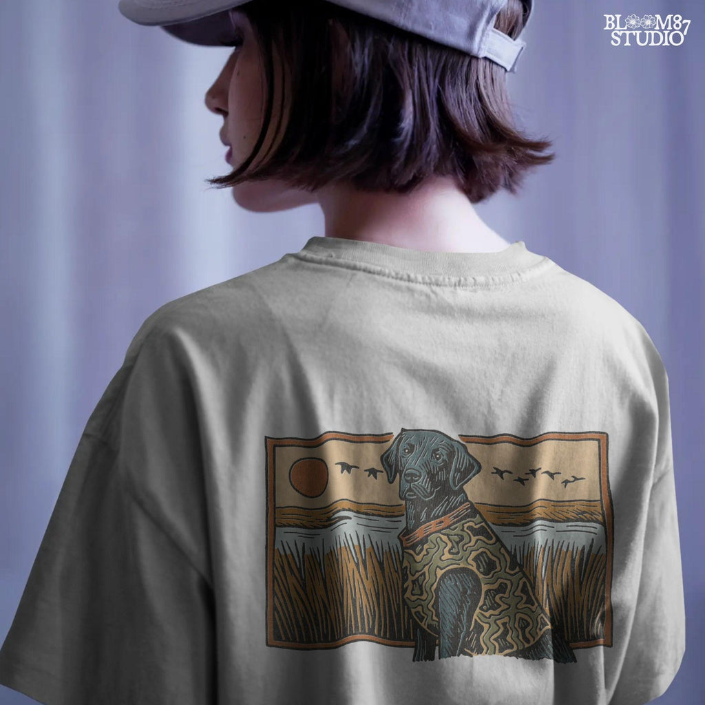 Camo-clad black Labrador retriever sitting in a grassy marsh with flying ducks and a sunset background, digital PNG for hunting dog sublimation designs.