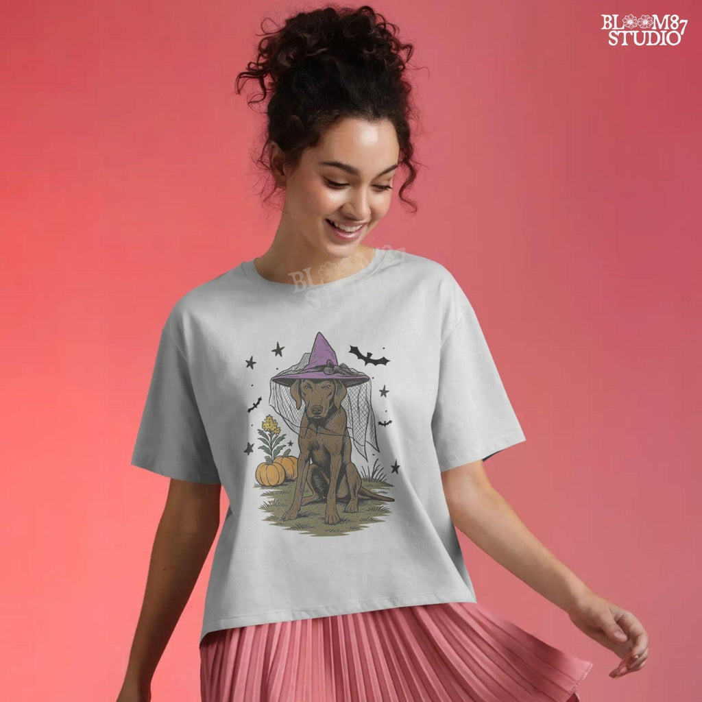 Illustration of a brown labrador wearing a witch hat, sitting in grass with pumpkins and stars in the background, in Halloween spooky style.