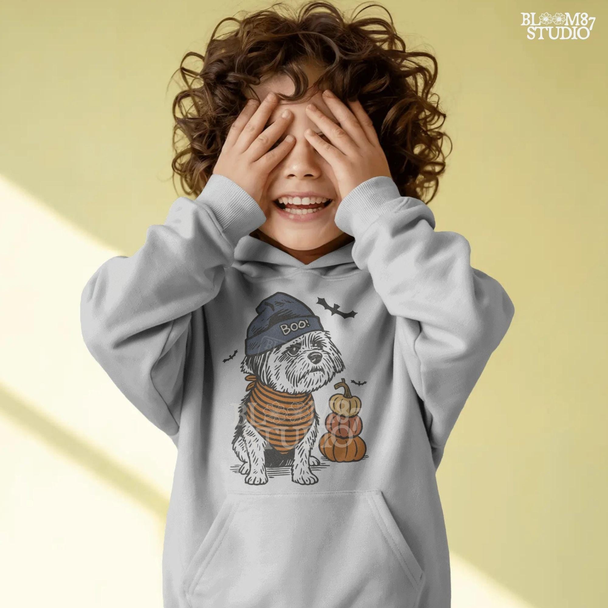 Illustration of a black dog wearing a “BOO!” hat and orange striped bandana, sitting next to stacked pumpkins on a Halloween background.