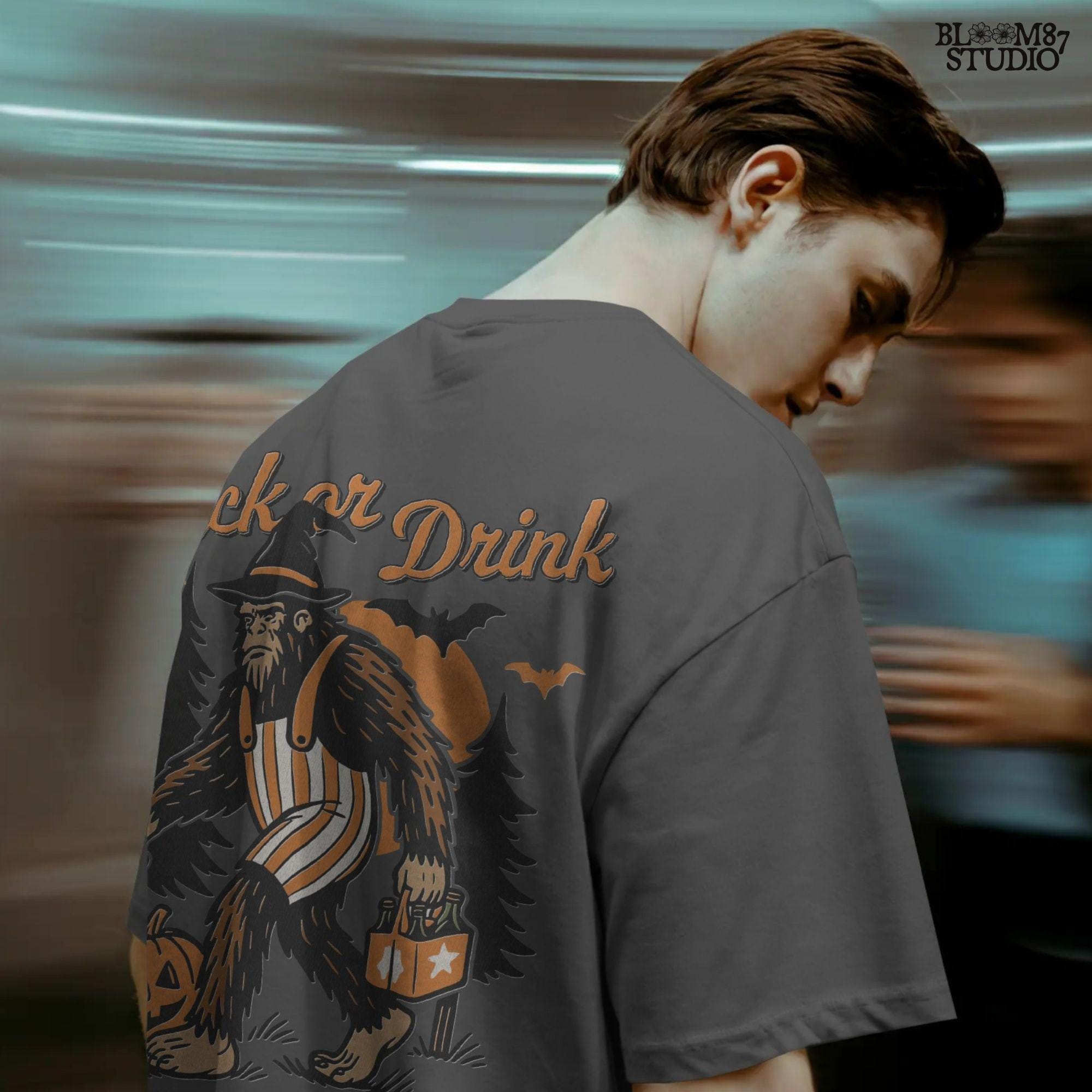 Funny Halloween bigfoot holding beer in witch hat and striped overalls, walking past pumpkins and trees with “Trick or Drink” text above.