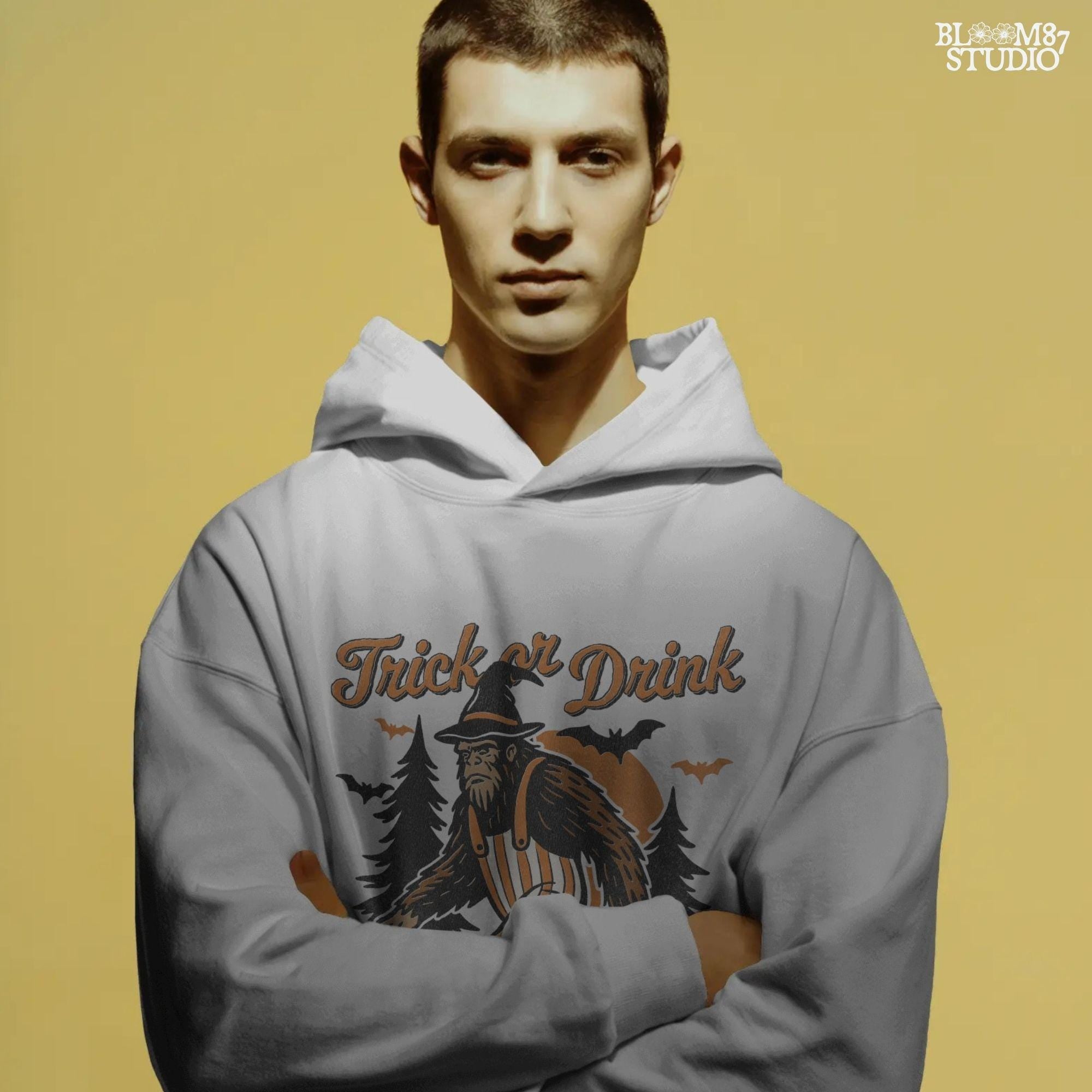 Funny Halloween bigfoot holding beer in witch hat and striped overalls, walking past pumpkins and trees with “Trick or Drink” text above.