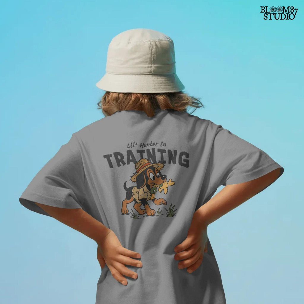 Cartoon hunting dog wearing straw hat and camo shirt holding duck toy in mouth with “Lil’ Hunter in Training” text – cute PNG for kids sublimation.