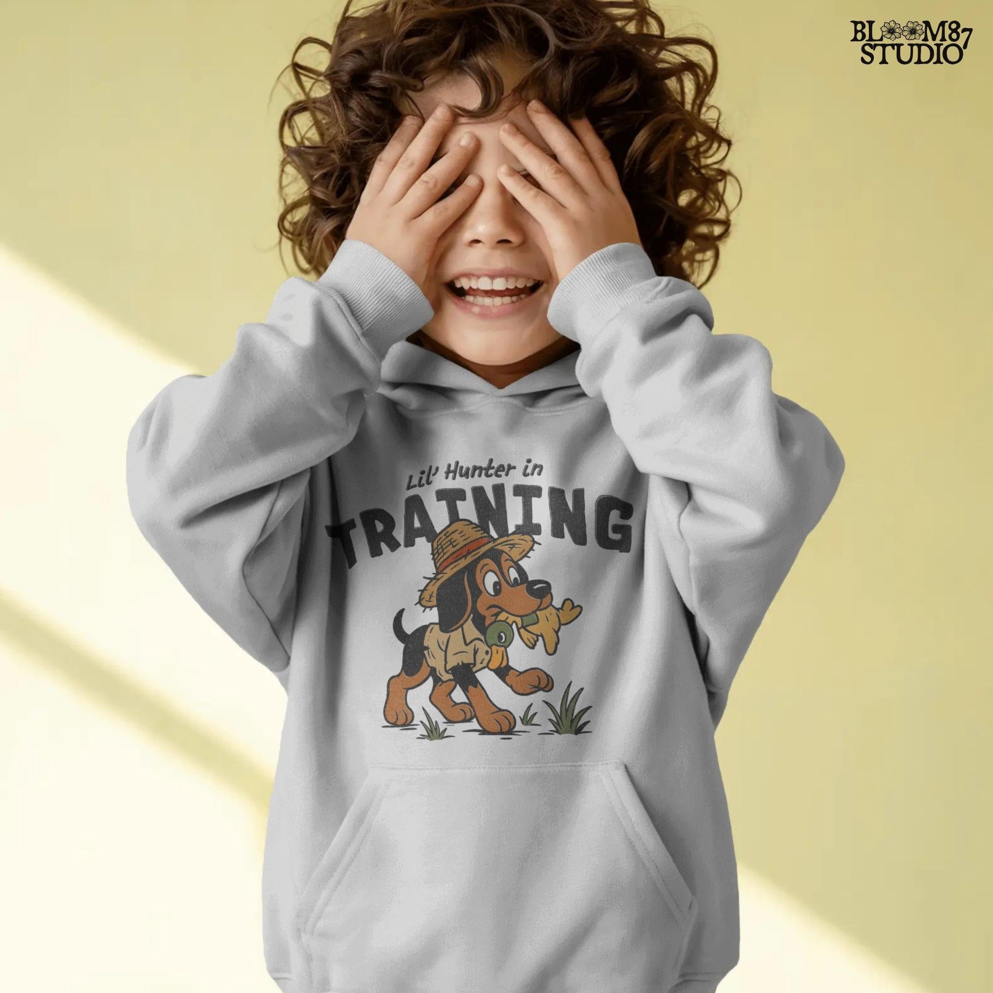 Cartoon hunting dog wearing straw hat and camo shirt holding duck toy in mouth with “Lil’ Hunter in Training” text – cute PNG for kids sublimation.