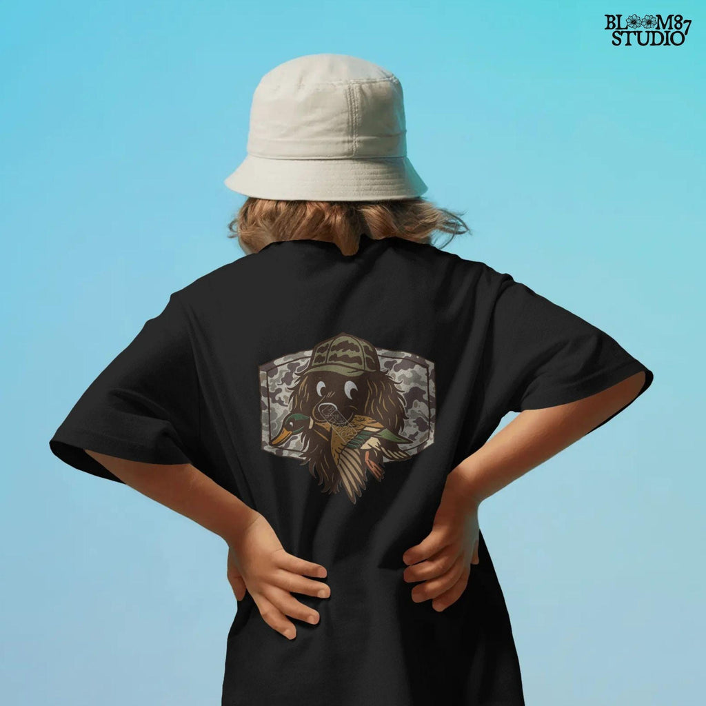 Cute cartoon hunting dog wearing camo hat holding a duck in its mouth with a camo background – sublimation PNG for boys or fall kids apparel design.