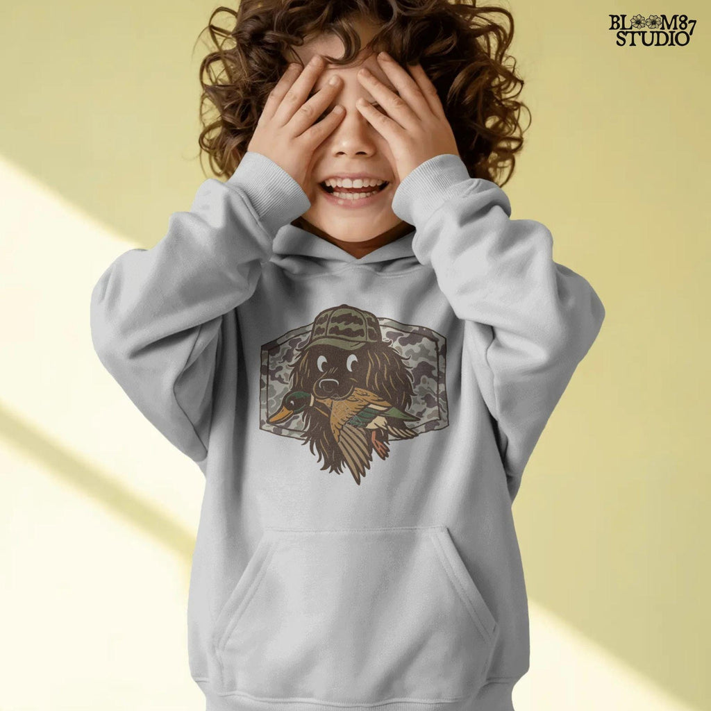 Cute cartoon hunting dog wearing camo hat holding a duck in its mouth with a camo background – sublimation PNG for boys or fall kids apparel design.