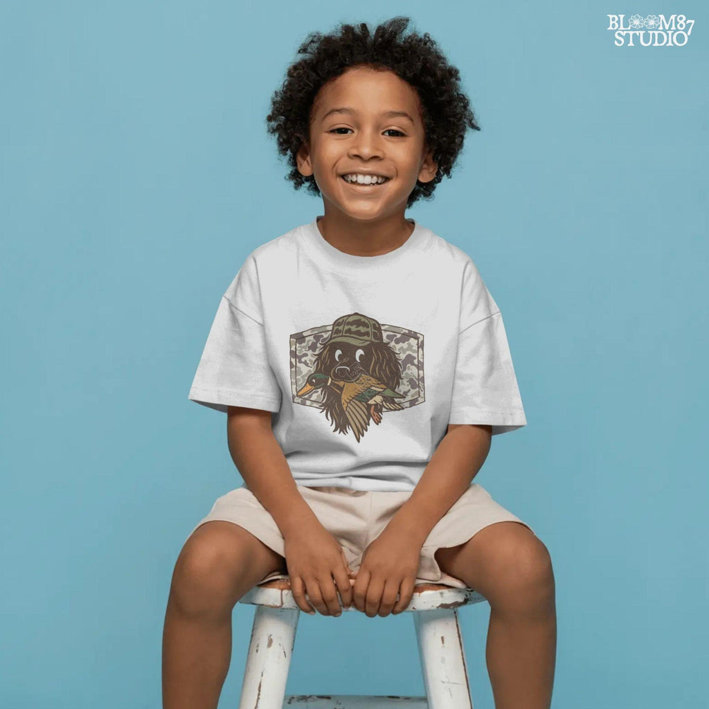 Cute cartoon hunting dog wearing camo hat holding a duck in its mouth with a camo background – sublimation PNG for boys or fall kids apparel design.