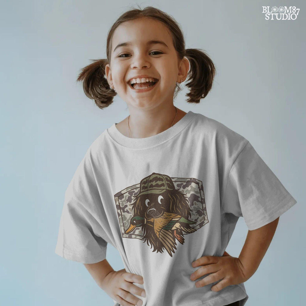 Cute cartoon hunting dog wearing camo hat holding a duck in its mouth with a camo background – sublimation PNG for boys or fall kids apparel design.