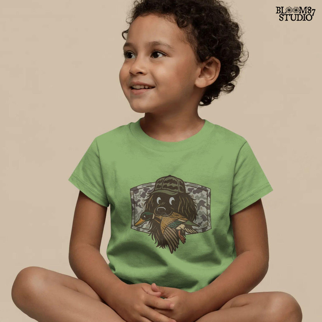 Cute cartoon hunting dog wearing camo hat holding a duck in its mouth with a camo background – sublimation PNG for boys or fall kids apparel design.