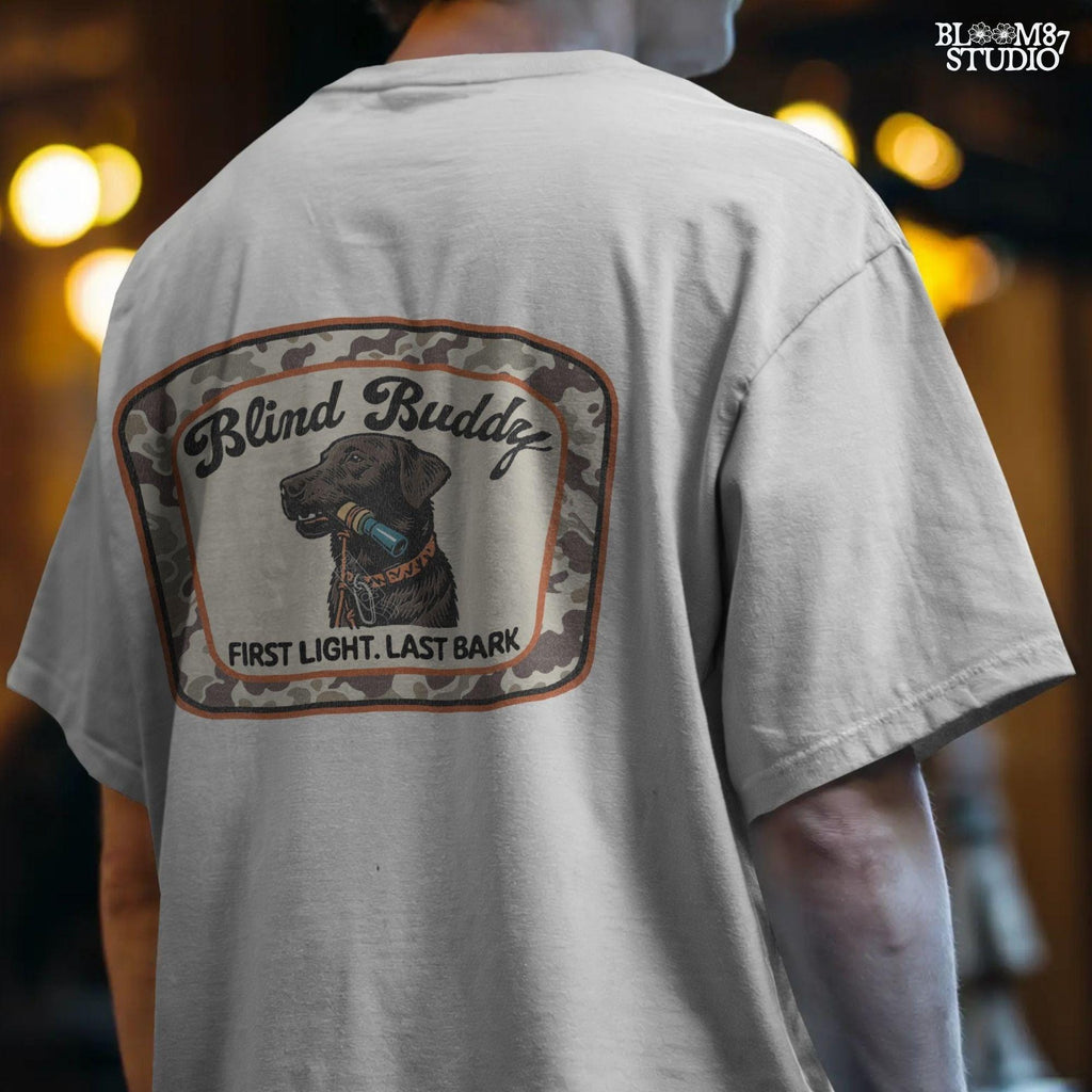 Black labrador dog holding a duck call in its mouth, centered in a camouflage hunting patch with text “Blind Buddy – First Light. Last Bark”