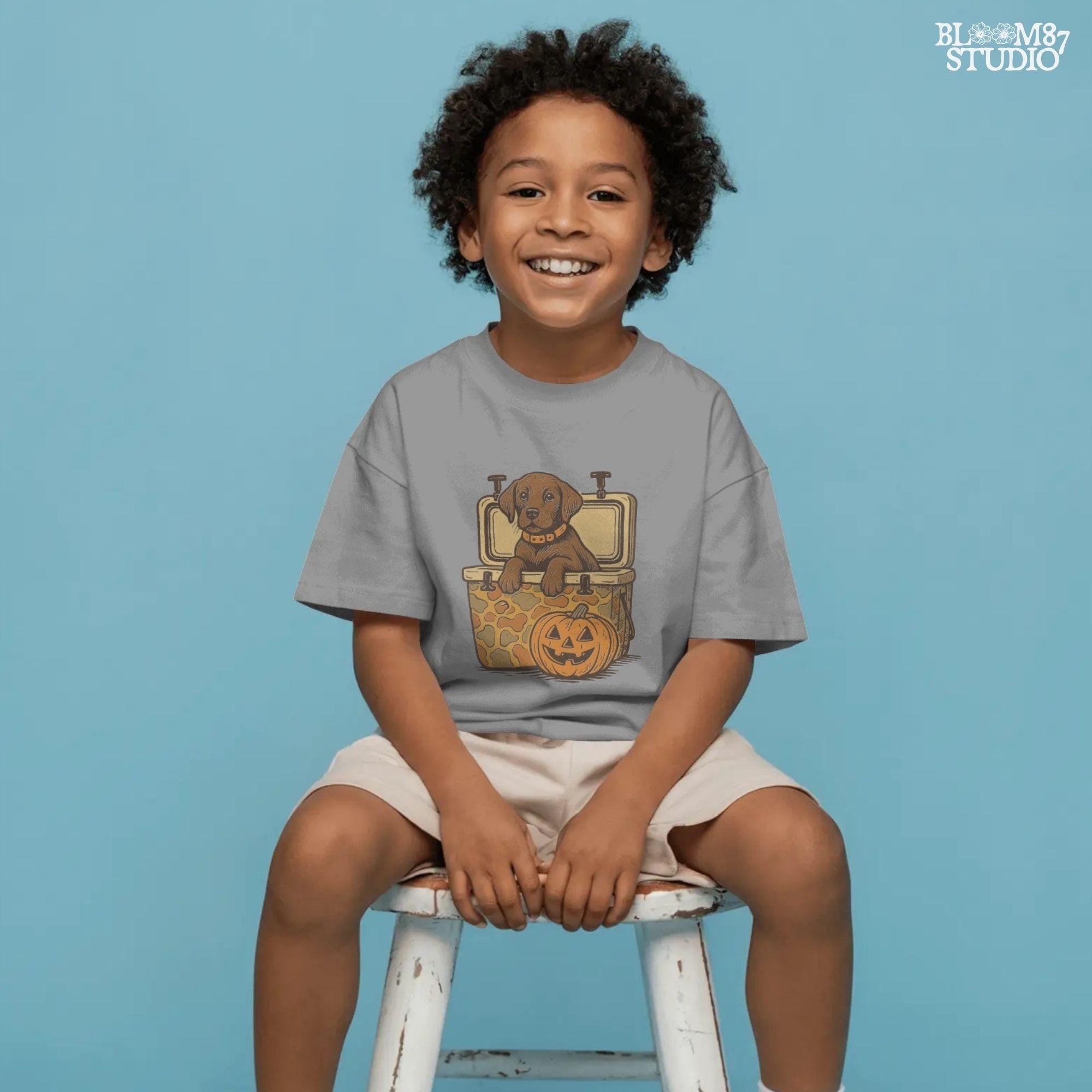 Cute brown hunting dog in a camo cooler next to a carved pumpkin, Halloween-themed sublimation PNG for fall shirts or seasonal crafts.