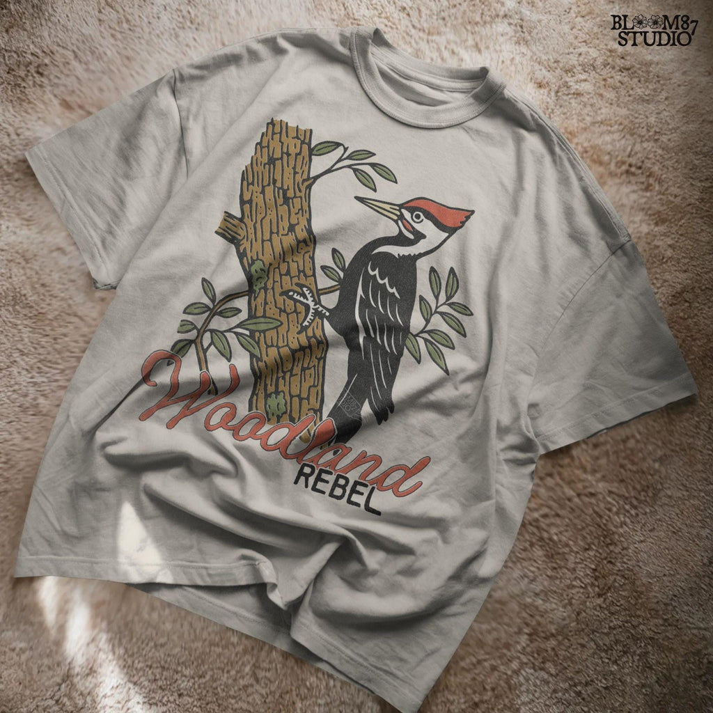 Vintage woodpecker perched on a tree trunk with green leaves and the word “Woodland” in rustic script, fall-themed forest sublimation PNG.