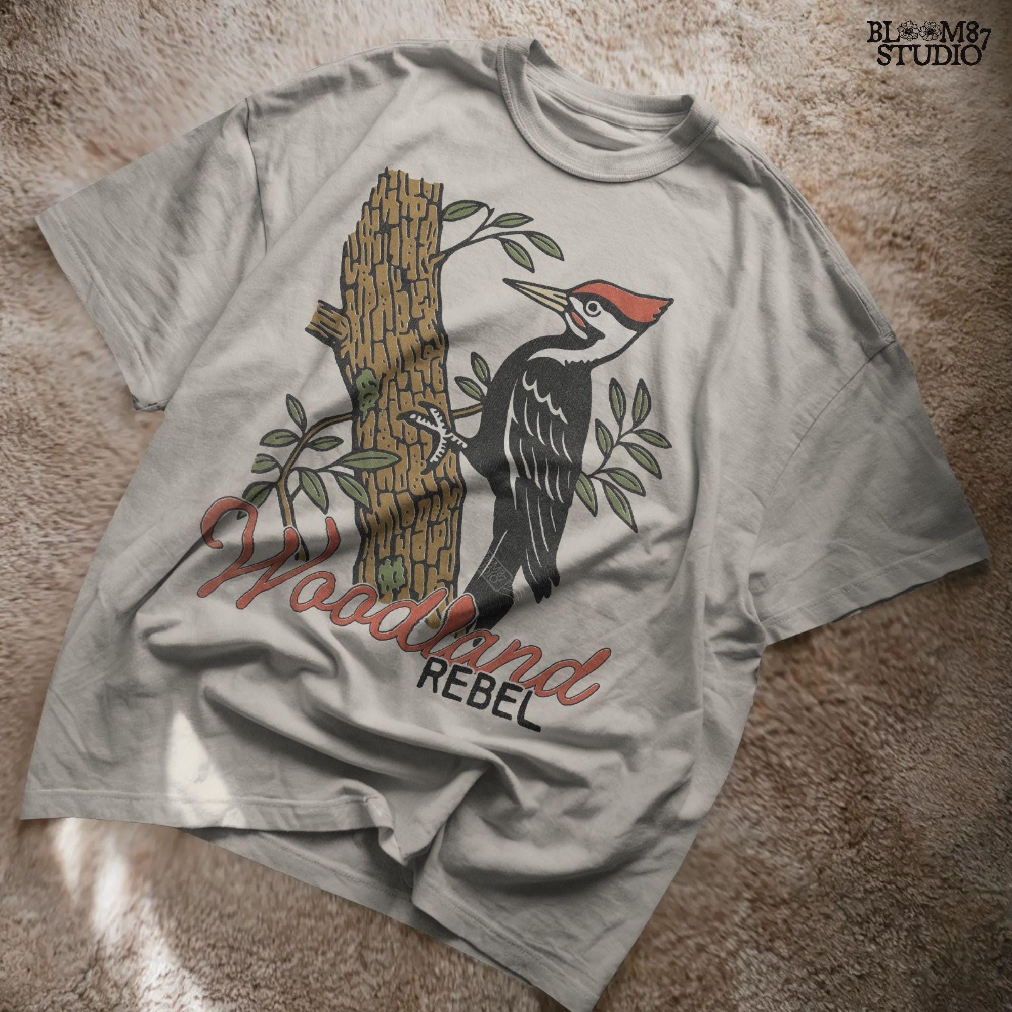Vintage woodpecker perched on a tree trunk with green leaves and the word “Woodland” in rustic script, fall-themed forest sublimation PNG.