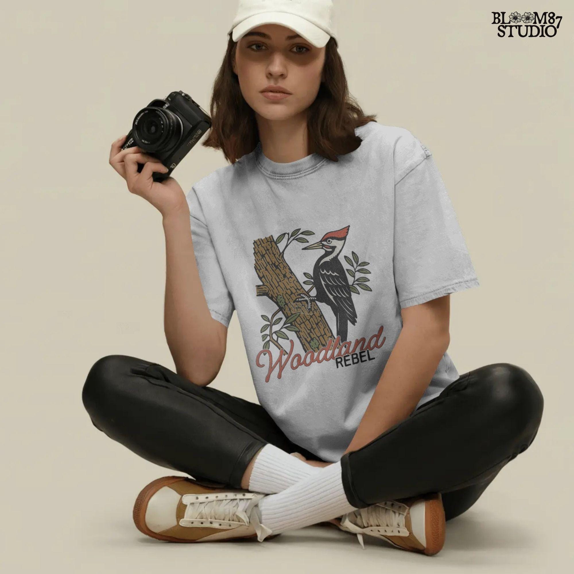Vintage woodpecker perched on a tree trunk with green leaves and the word “Woodland” in rustic script, fall-themed forest sublimation PNG.