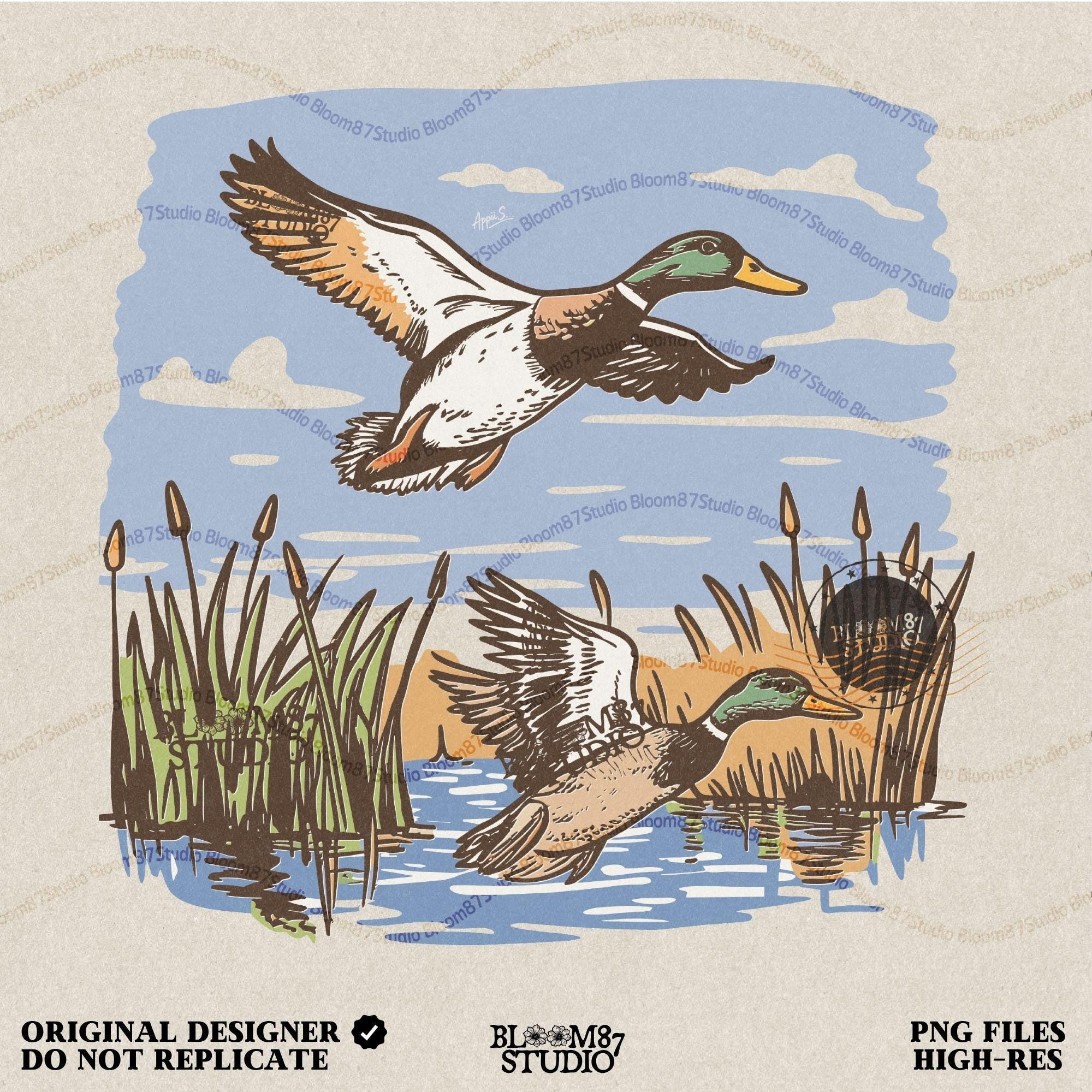 May include: A beige t-shirt with a graphic print of two ducks flying over a pond with reeds. The ducks are brown and green and the pond is blue. The reeds are green and brown. The t-shirt has a crew neck and short sleeves.