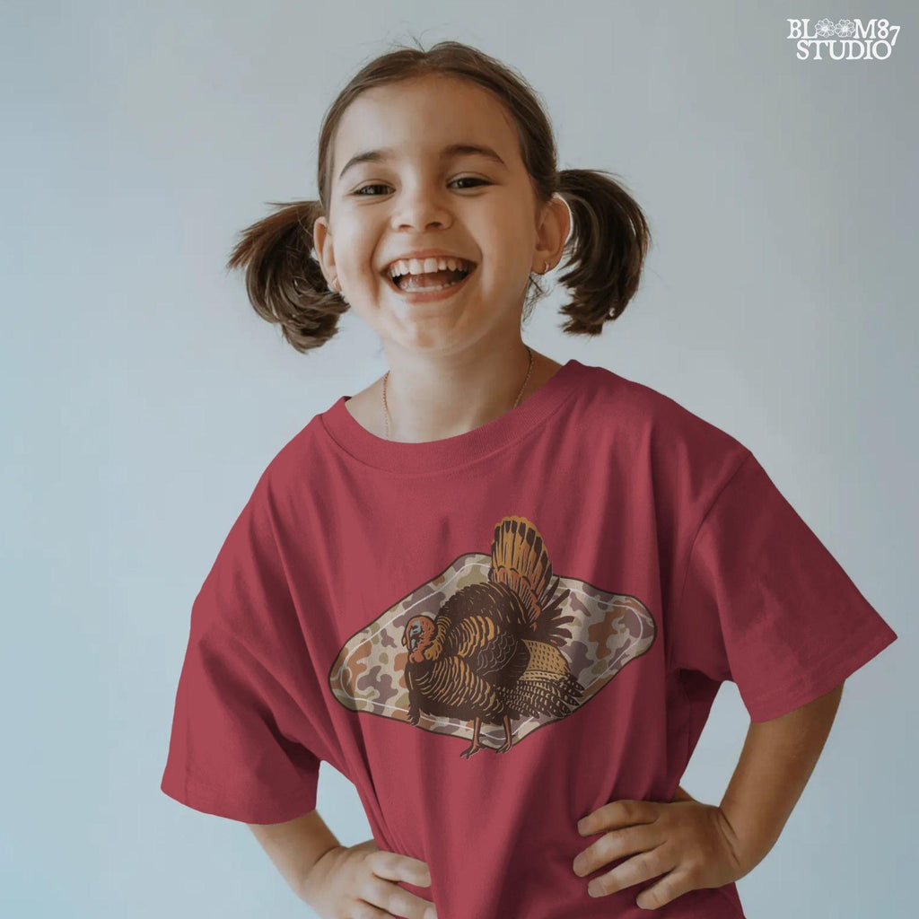 Illustration of a wild turkey with full plumage standing over a tan woodland camouflage background, ideal for fall or Thanksgiving sublimation designs.