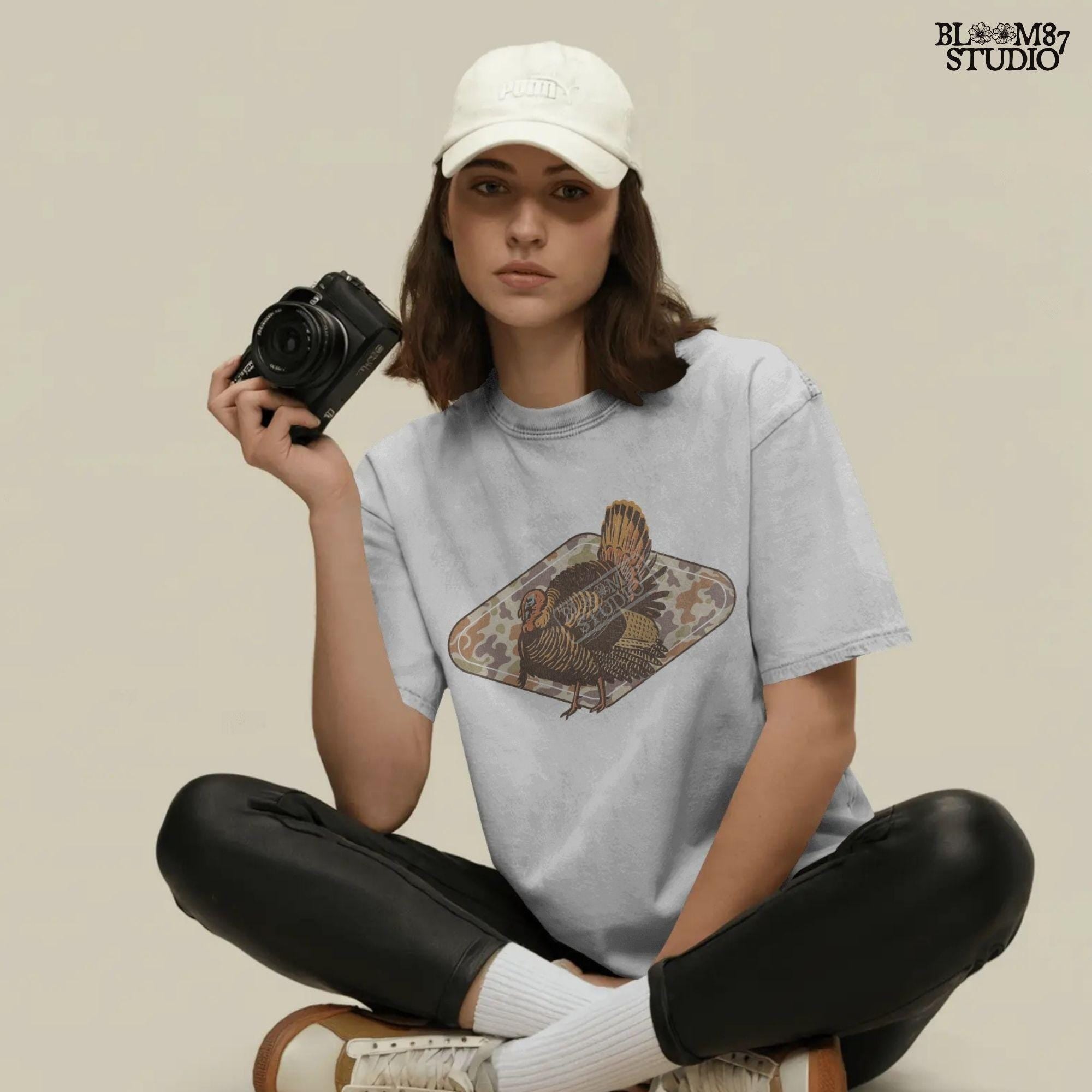 Illustration of a wild turkey with full plumage standing over a tan woodland camouflage background, ideal for fall or Thanksgiving sublimation designs.