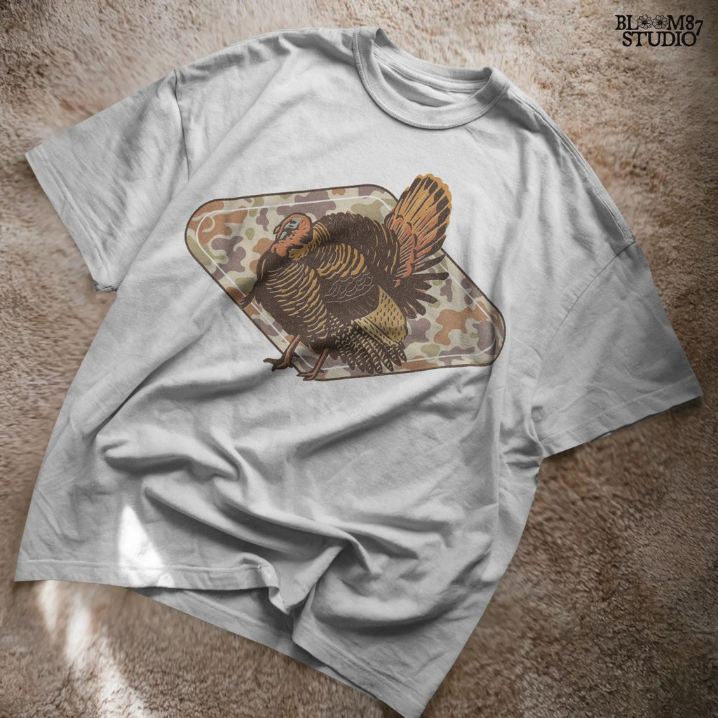 Illustration of a wild turkey with full plumage standing over a tan woodland camouflage background, ideal for fall or Thanksgiving sublimation designs.