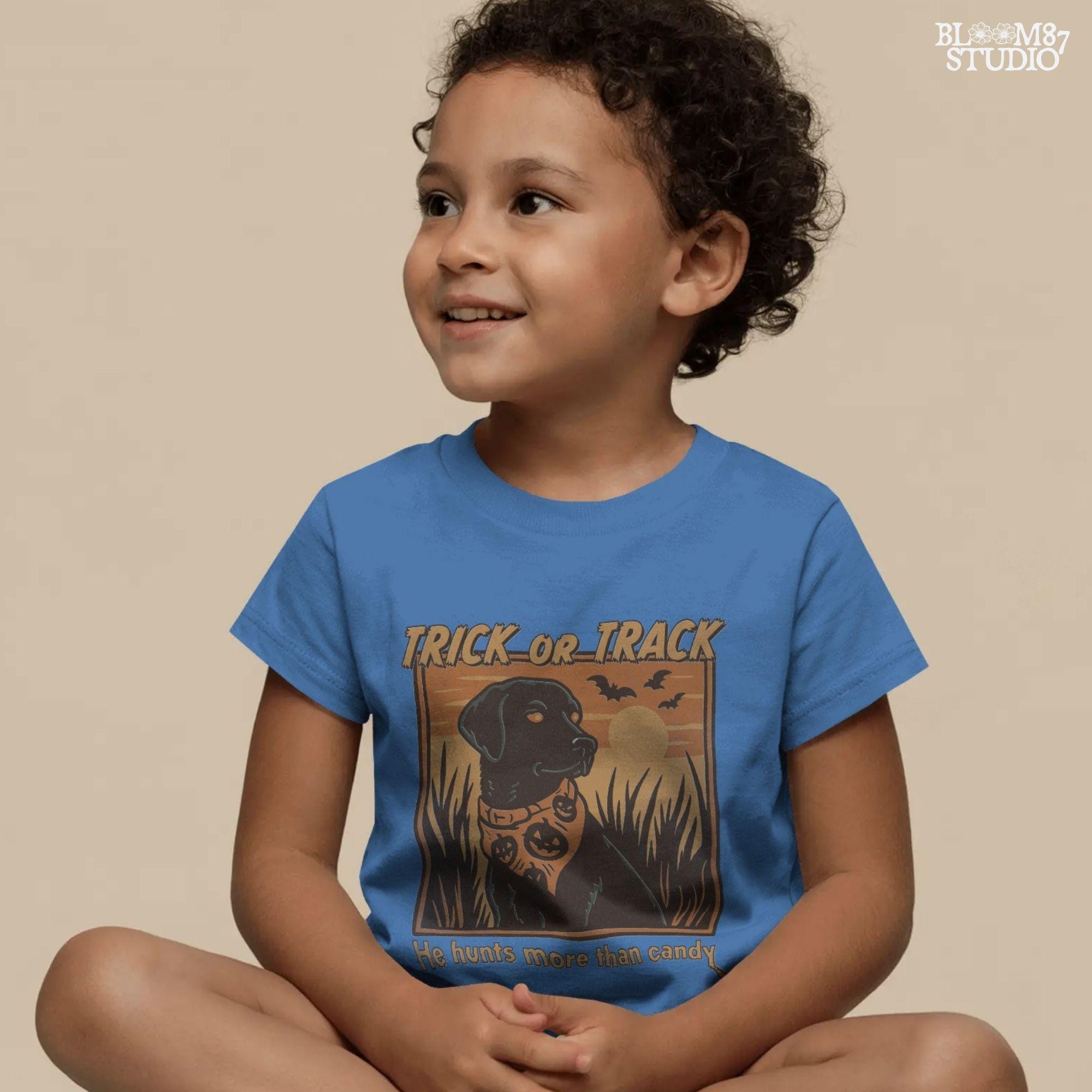 Halloween PNG of a black lab hunting dog wearing a pumpkin bandana with bats, sunset, and text “Trick or Track – He Hunts More Than Candy”