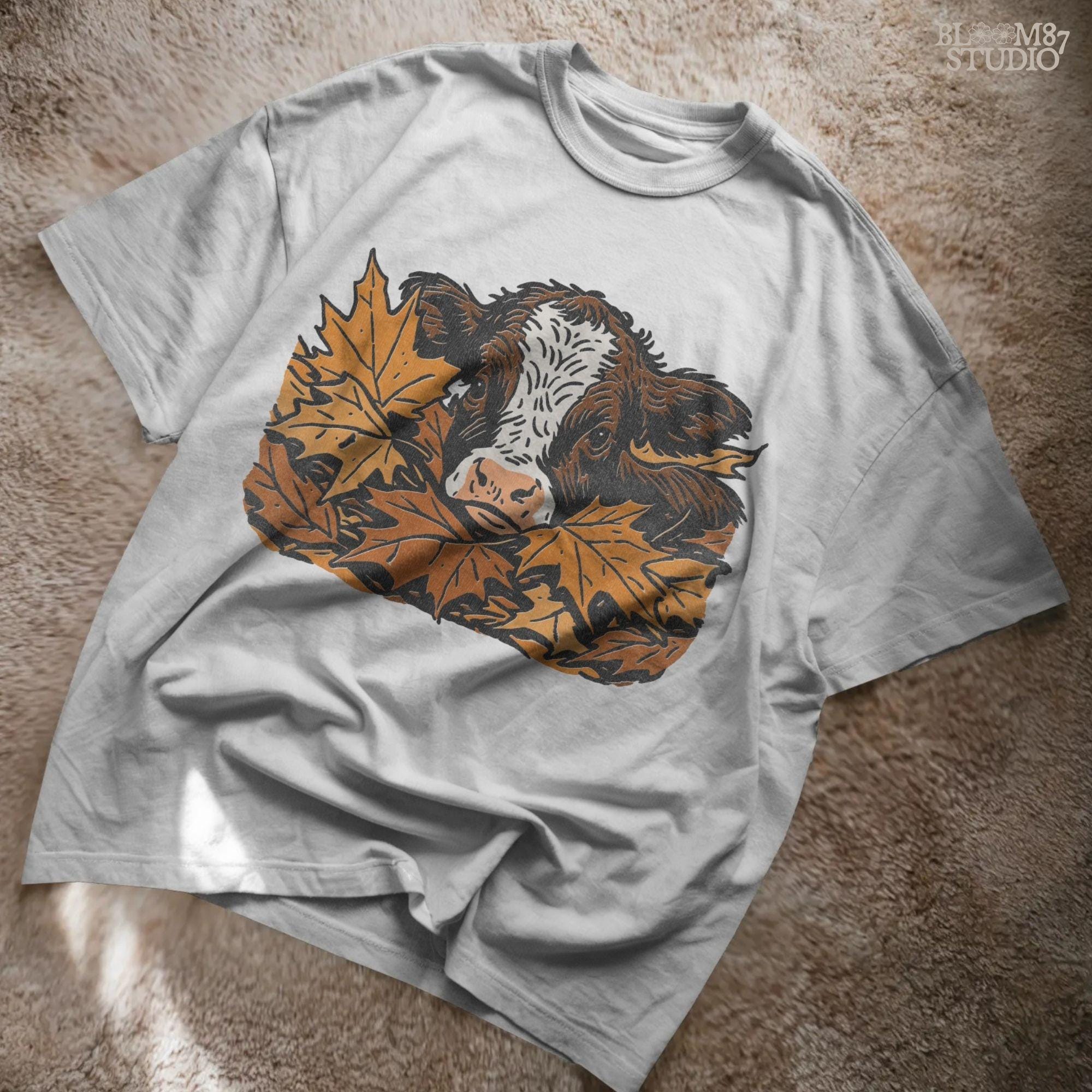 Cute brown and white highland calf resting in a pile of orange and brown fall maple leaves, perfect for autumn sublimation projects