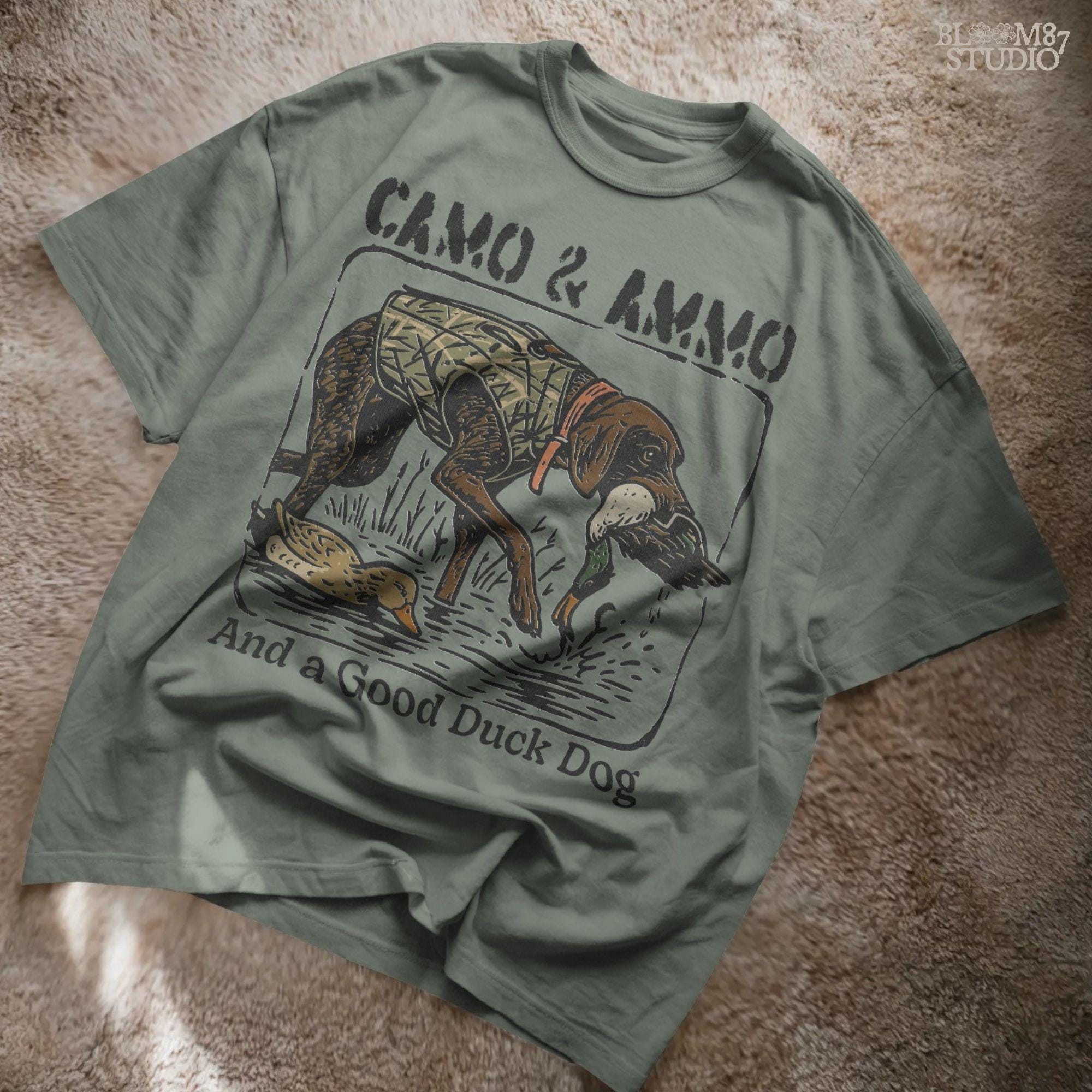 Hunting dog in a camo vest retrieving a mallard duck with a swimming duck nearby and text saying “Camo & Ammo and a Good Duck Dog”.