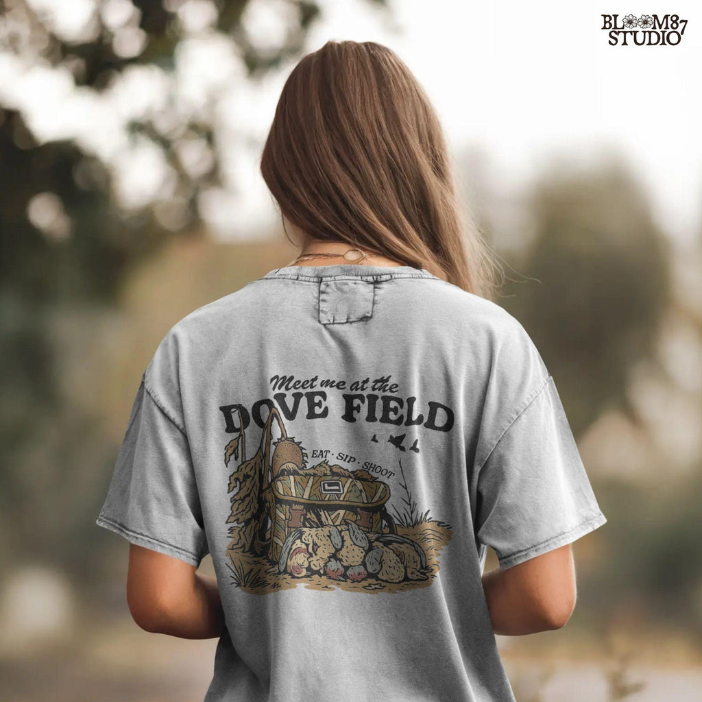 Camo hunting bag in a cornfield surrounded by harvested mourning doves with the phrase “Meet Me at the Dove Field” in vintage lettering.