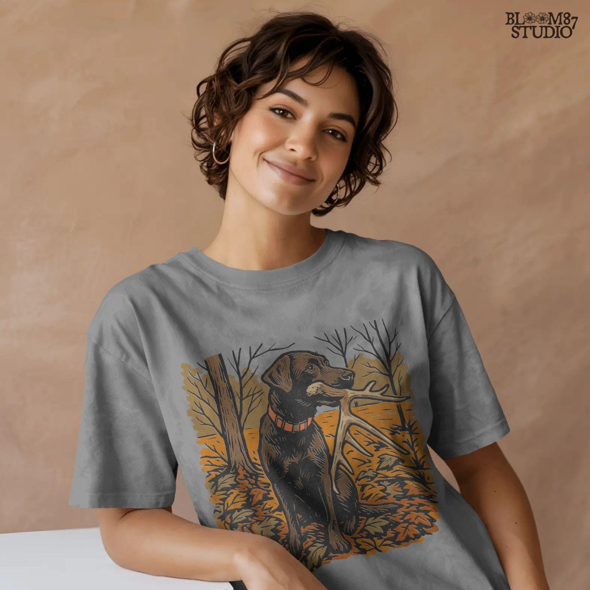 Illustration of a black Labrador dog sitting in autumn leaves holding a deer antler in its mouth, rustic hunting sublimation PNG design.