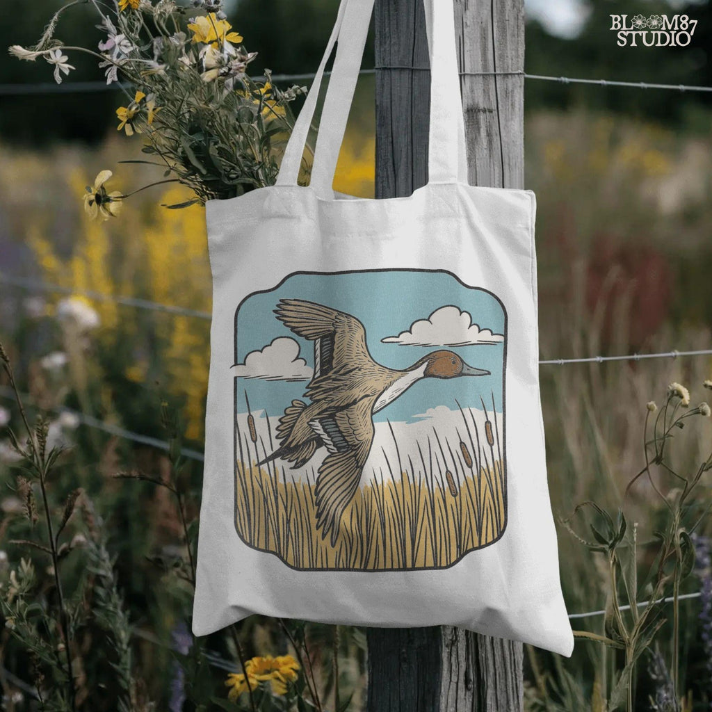 Illustration of a pintail duck flying above cattails with a blue sky and clouds, rustic waterfowl hunting sublimation PNG design.