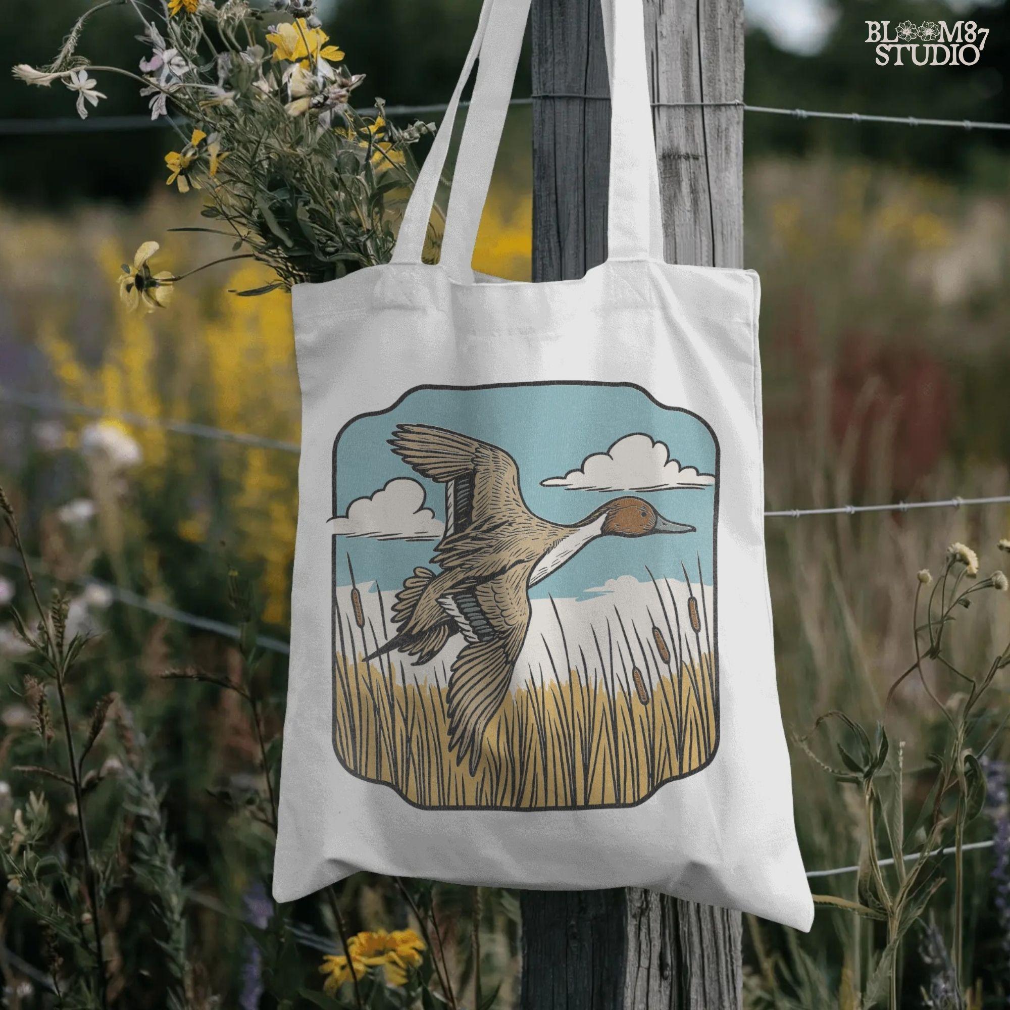 Illustration of a pintail duck flying above cattails with a blue sky and clouds, rustic waterfowl hunting sublimation PNG design.