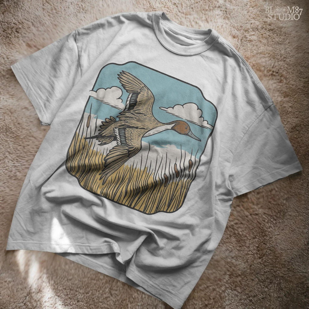 Illustration of a pintail duck flying above cattails with a blue sky and clouds, rustic waterfowl hunting sublimation PNG design.