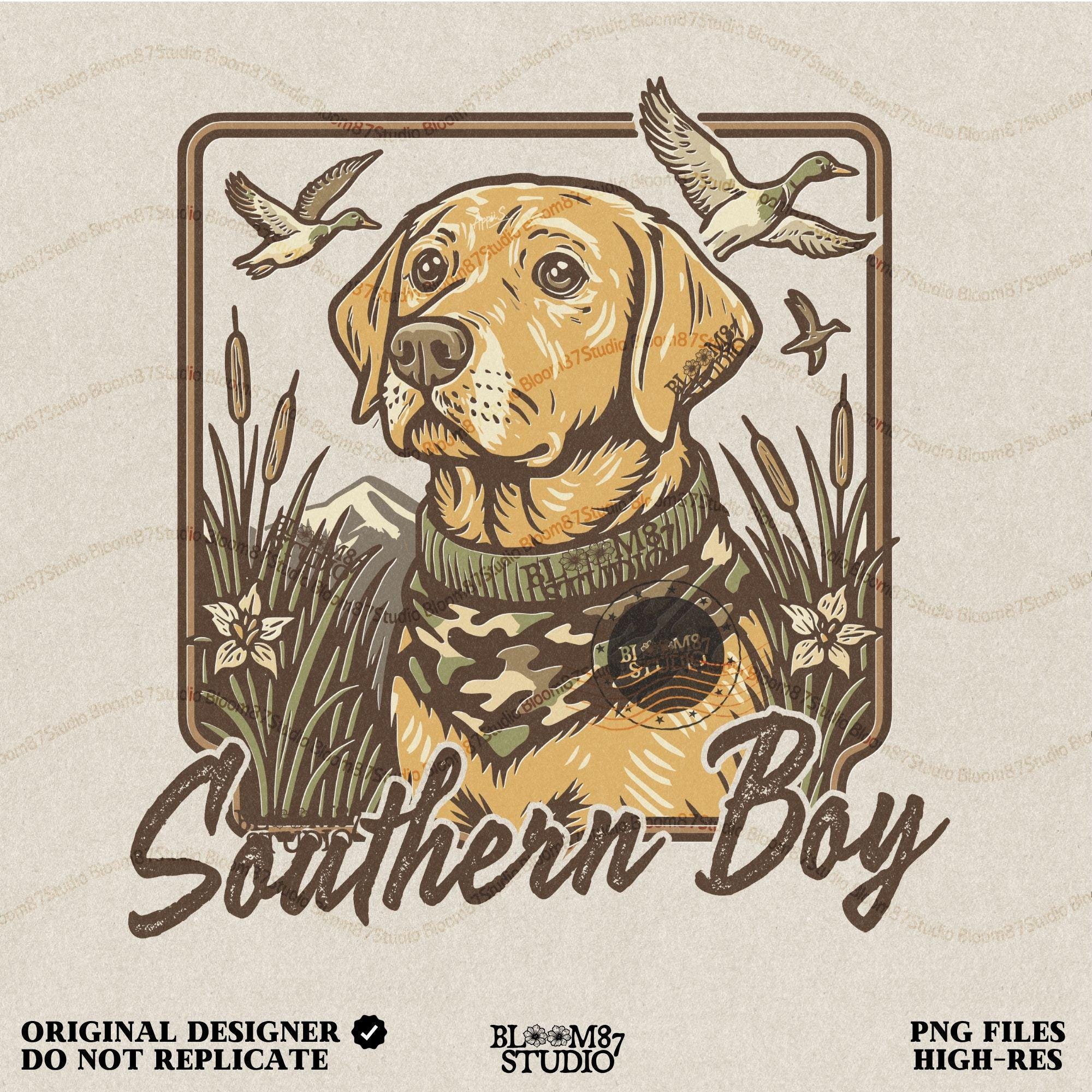 May include: A person wearing a light gray t-shirt with a brown and yellow illustration of a dog wearing a camouflage scarf. The illustration is surrounded by a brown frame and the text 'Southern Boy' is printed below the dog.