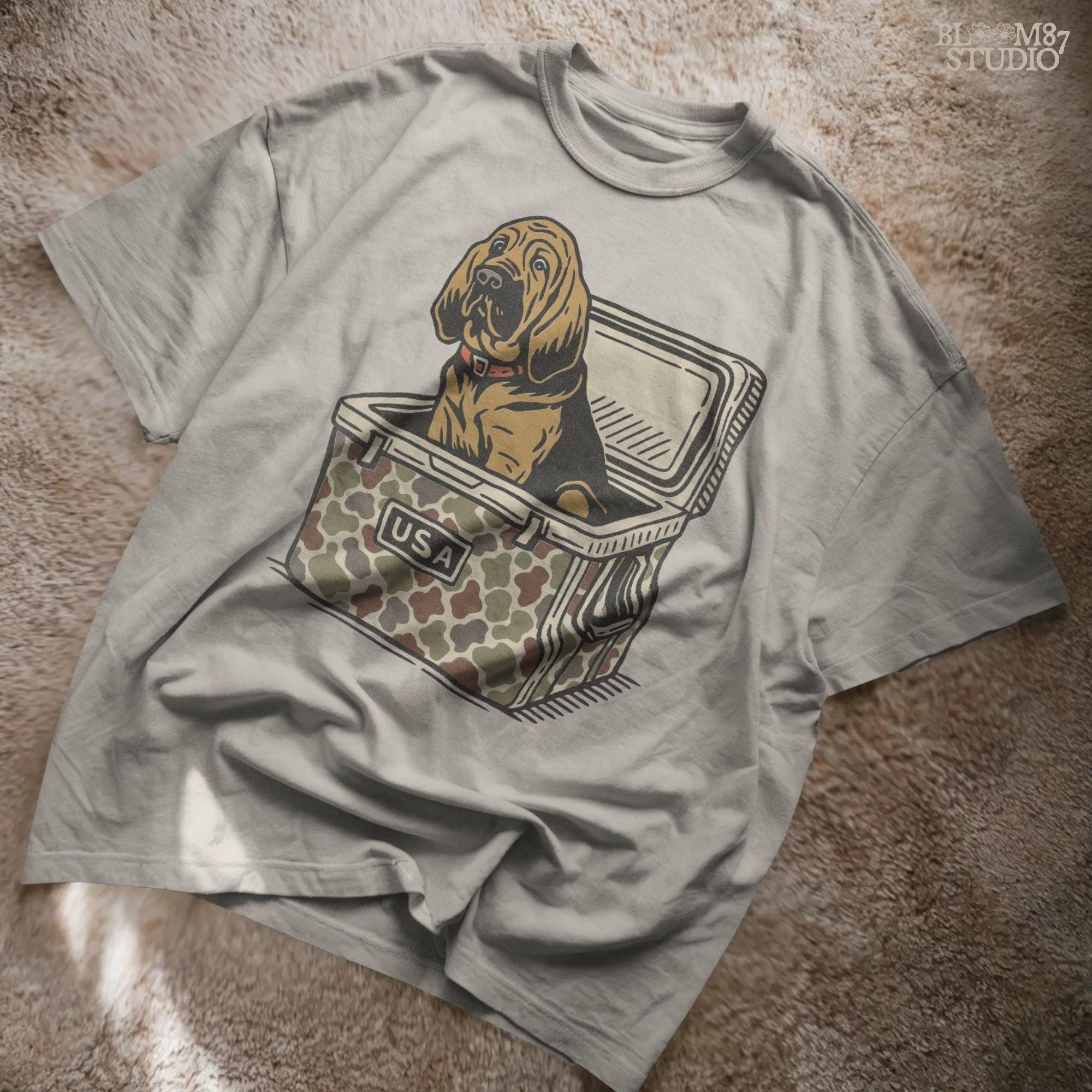 Illustration of a brown bloodhound dog sitting inside a camouflage cooler with “USA” label, hunting and outdoor-themed sublimation PNG design