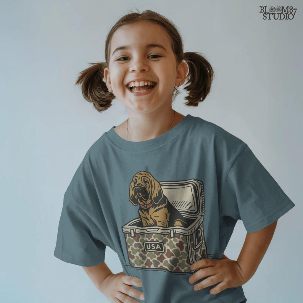 Illustration of a brown bloodhound dog sitting inside a camouflage cooler with “USA” label, hunting and outdoor-themed sublimation PNG design