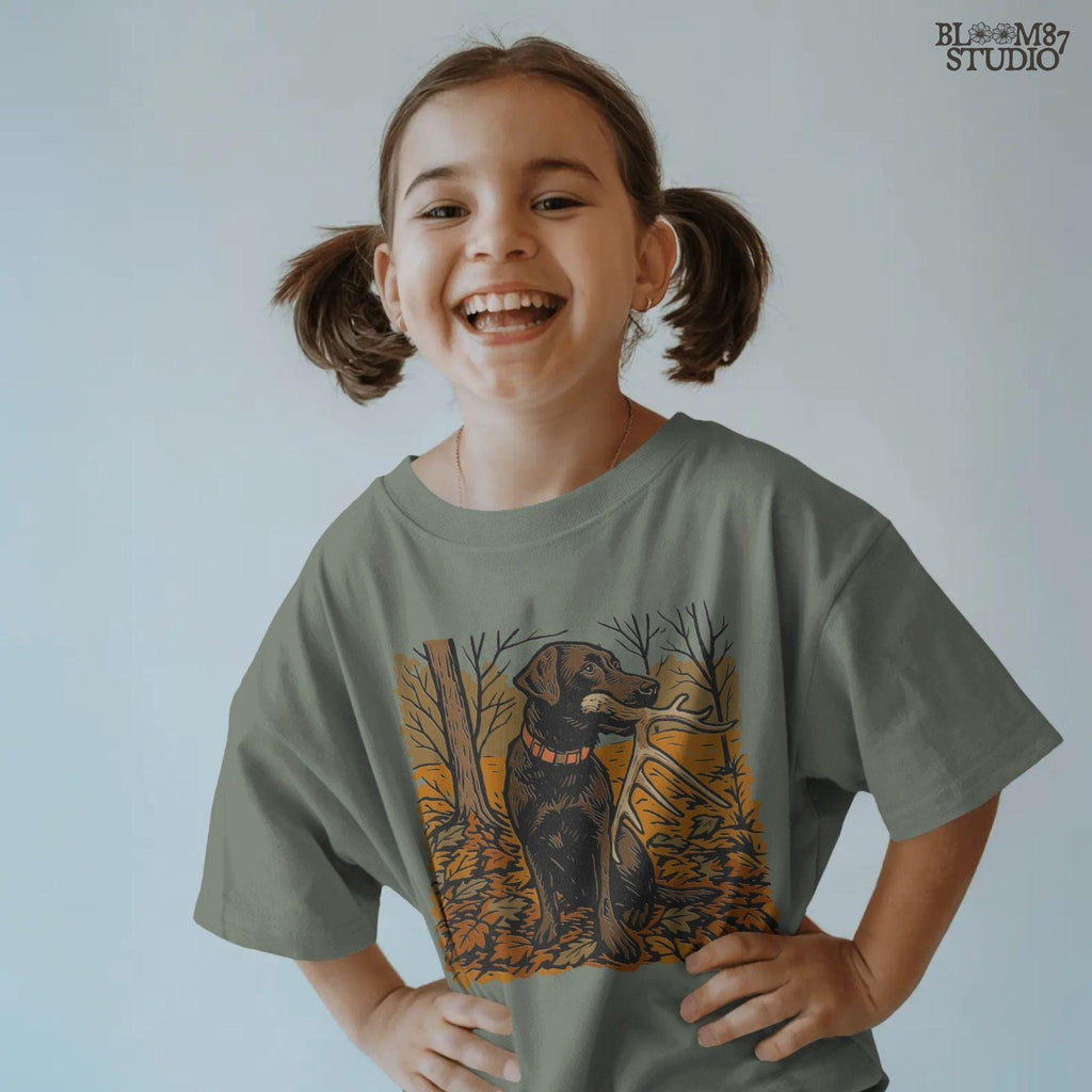 Illustration of a black Labrador dog sitting in autumn leaves holding a deer antler in its mouth, rustic hunting sublimation PNG design.