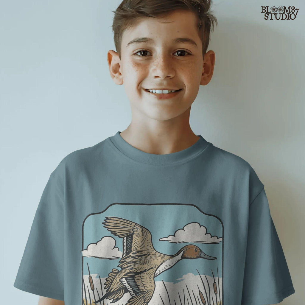 Illustration of a pintail duck flying above cattails with a blue sky and clouds, rustic waterfowl hunting sublimation PNG design.