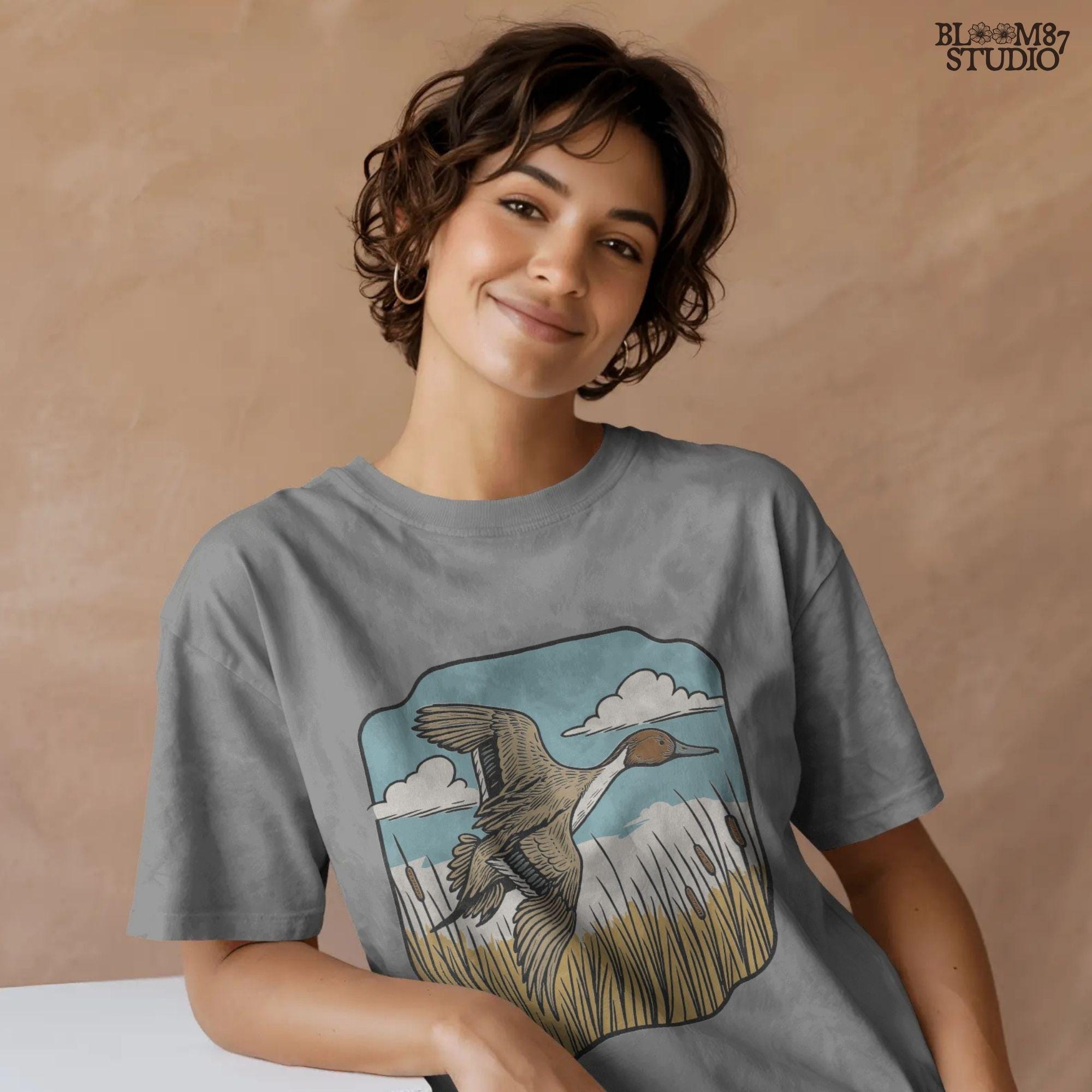 Illustration of a pintail duck flying above cattails with a blue sky and clouds, rustic waterfowl hunting sublimation PNG design.