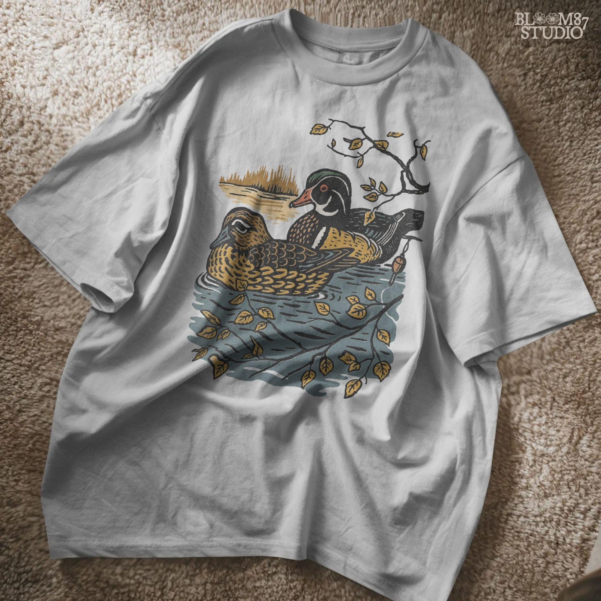 Vintage illustration of a wood duck couple floating on a pond, surrounded by fall leaves and branches, ideal for rustic nature sublimation.

Distressed Version:
Distressed wood duck pair in a peaceful pond setting with autumn leaves, perfect for farmhouse wildlife crafts and romantic outdoor art.