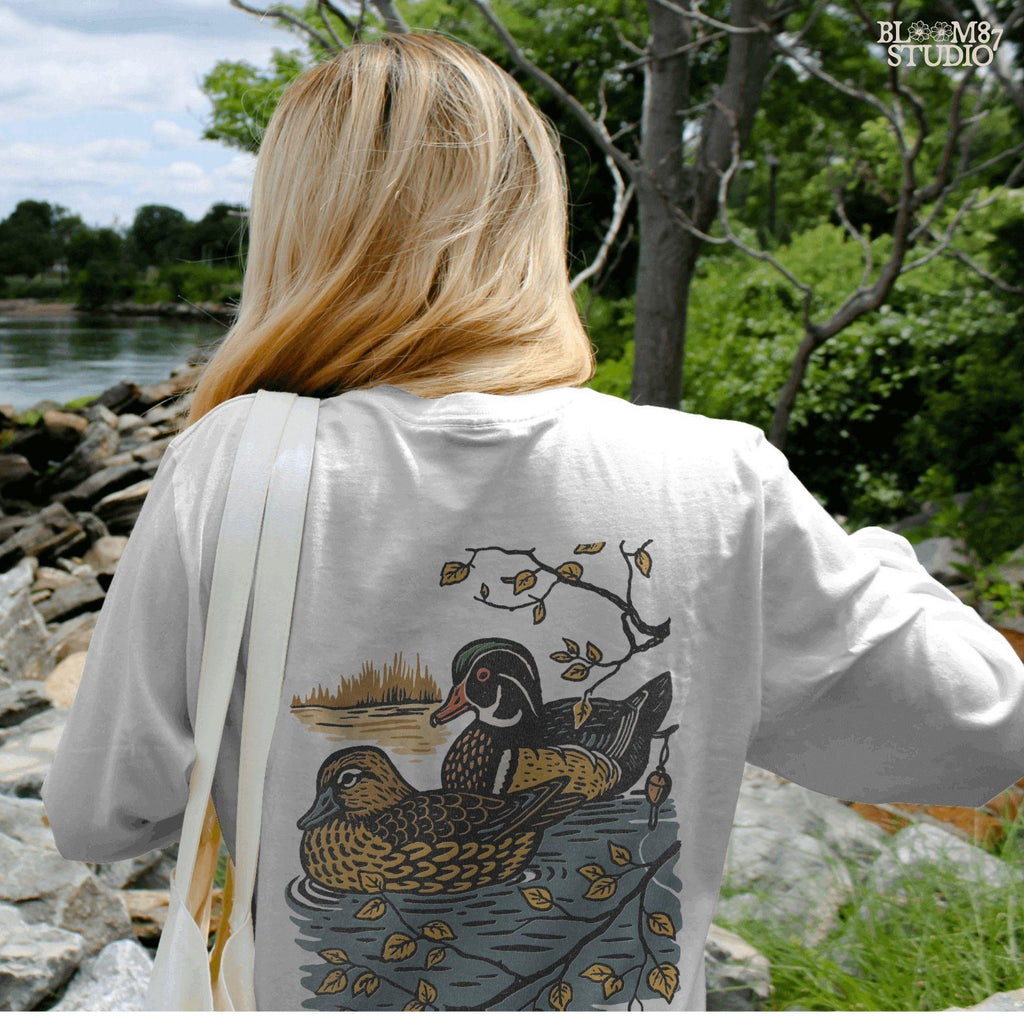 Vintage illustration of a wood duck couple floating on a pond, surrounded by fall leaves and branches, ideal for rustic nature sublimation.

Distressed Version:
Distressed wood duck pair in a peaceful pond setting with autumn leaves, perfect for farmhouse wildlife crafts and romantic outdoor art.