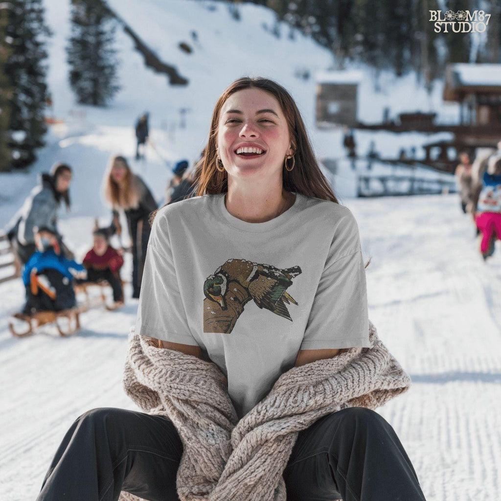 Solid Version:
Realistic illustration of a dead duck lying on a camo arm with snow on its feathers, vintage sublimation PNG for winter hunting themes.

Distressed Version:
Distressed-style snowy duck laying across a hunting jacket, ideal for rustic sublimation and cold season outdoor craft designs.