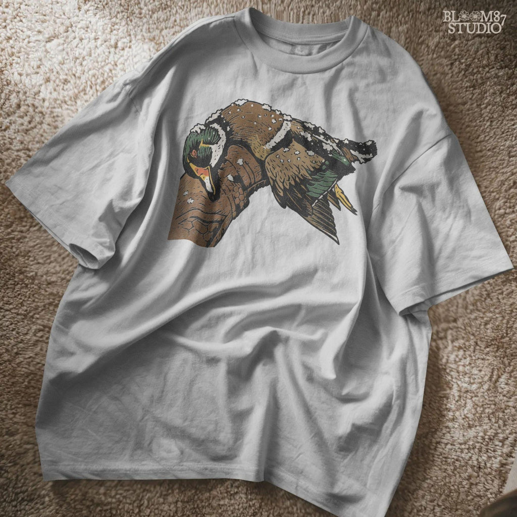Solid Version:
Realistic illustration of a dead duck lying on a camo arm with snow on its feathers, vintage sublimation PNG for winter hunting themes.

Distressed Version:
Distressed-style snowy duck laying across a hunting jacket, ideal for rustic sublimation and cold season outdoor craft designs.