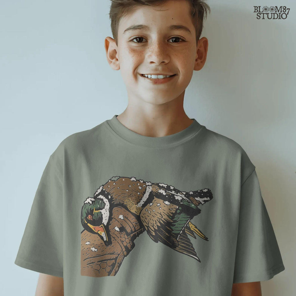 Solid Version:
Realistic illustration of a dead duck lying on a camo arm with snow on its feathers, vintage sublimation PNG for winter hunting themes.

Distressed Version:
Distressed-style snowy duck laying across a hunting jacket, ideal for rustic sublimation and cold season outdoor craft designs.
