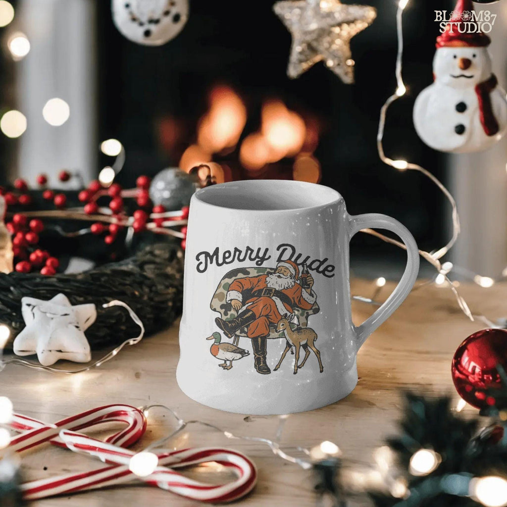 Cartoon Santa sitting on a camo patterned chair holding soda, deer and duck around him, Merry Dude lettering. Digital download for Christmas shirts, mugs, Santa camo hunting designs, and festive home decor.
